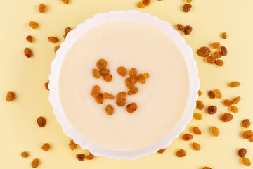 Semolina porridge with raisins in a white plate (bowl) on a yellow background close-up. Contains gluten. Healthy children's breakfast.