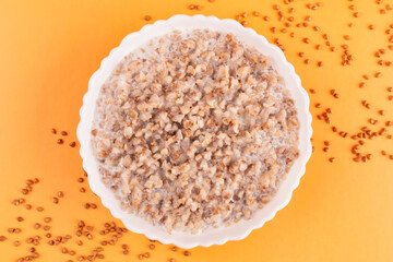 Buckwheat porridge with milk in a white bowl (plate) on an orange background. Healthy breakfast. Porridge for a child (baby).