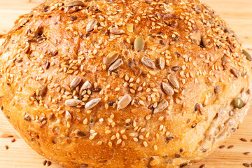 Round bread made of whole wheat flour with pumpkin seeds, sesame seeds, flax and sunflower seeds on a wooden background. Recipe. Bread without yeast, with sourdough. Proper nutrition.