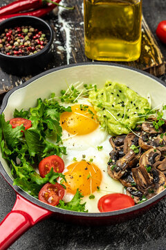 Fried scrambled eggs in a frying pan with avocado and mushrooms on a light background. Keto diet. vertical image. top view. place for text