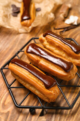 Grid with tasty chocolate eclairs on wooden table, closeup