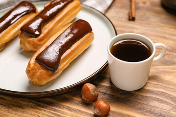 Plate with tasty chocolate eclairs and cup of coffee on wooden table, closeup