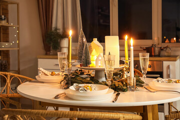 Christmas table setting with candle holders and fir trees in kitchen at night