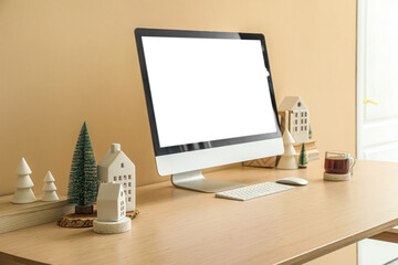 Workplace with computer, candle holders and Christmas trees near beige wall