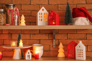 Shelves with candle holders, Christmas trees and Santa hat on brick wall