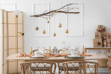 Interior of light room with dining table, tree branches and Christmas balls