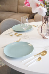 Round dining table in modern apartment, table setting with flowers for a casual dinner party. 