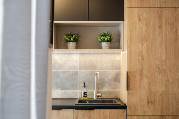 Kitchen in a modern mix of natural wood and black panels. Kitchen faucet and dish soap dispenser