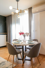 Round dining table in modern apartment, table setting with flowers for a casual dinner party. 