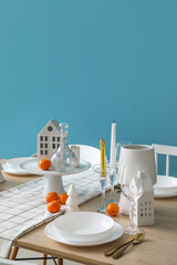 Christmas table setting with candle holders and mandarins near blue wall
