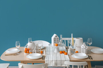 Christmas table setting with candle holders and mandarins near blue wall