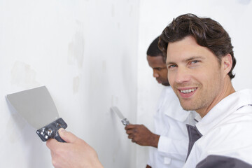 two builders in overalls with spatula repairing wall