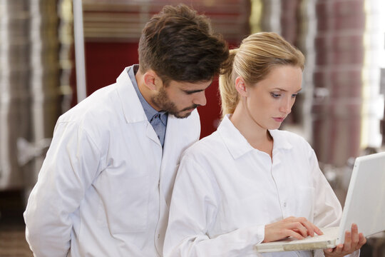 colleagues wearing labcoats looking at laptop in brewery
