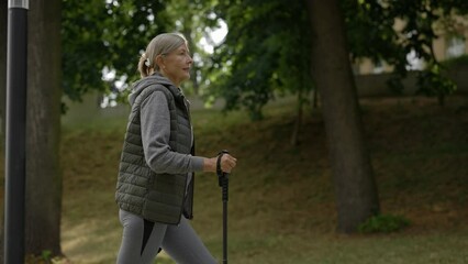 Mature caucasian woman training nordic walking with ski trekking poles in park. Active leisure. Aging youthfully. People and sport concept.