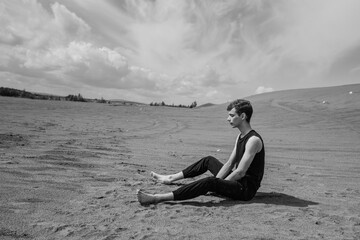 Fototapeta premium Lone man sitting barefoot on the sand in sandy desert