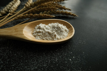Close-up golden ears of wheat, a spoon and scattered flour on a black background