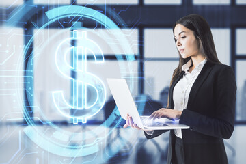 Attractive young european businesswoman using laptop with glowing dollar sign on blurry office...