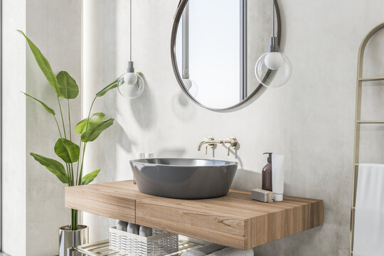 Perspective view on wooden sink cabinet with round mirror above and concrete wall background in loft style sunlit bathroom. 3D rendering