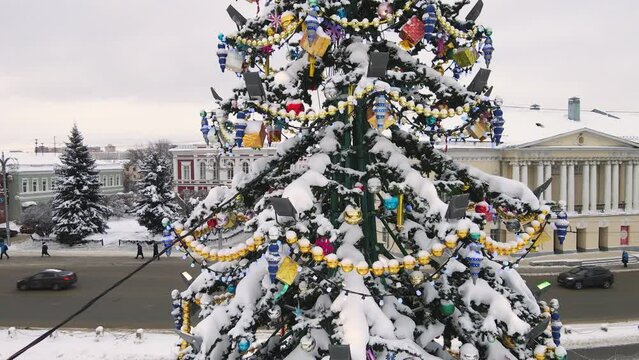 Aerial view, close-up of toys and flashing garlands on a Christmas tree. New Year's, green spruce fabulously decorated and covered with snow. City of Vladimir, Cathedral Square, Russia. UHD 4K.
