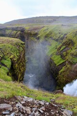 Fototapeta na wymiar Majestic Icelandic Water fall with green moss and Lava rocks between cliff formation. damp fresh icelandic landscape with strong green and earth tones
