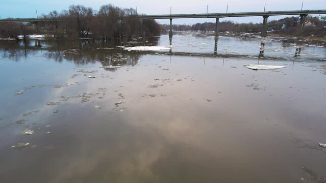 Automobile bridge across a gloomy river stream with floating ice floes. Spring, snow melts, ice drift, flood and flood of the river. Day, cloudy weather, soft warm light. UHD 4K