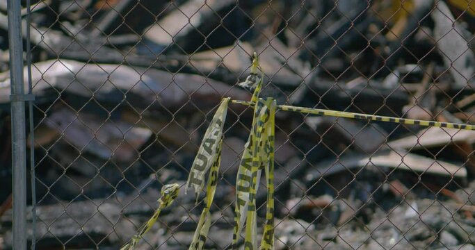 Burnt down bar restaurant or house from ground level yellow caution tape as camera pulls focus through Chainlink fence to fire damage wreckage.
