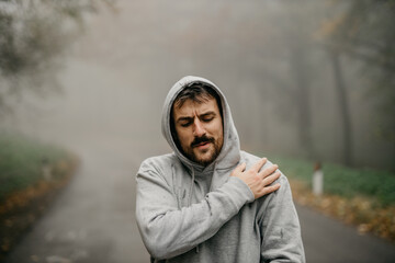Young Caucasian athletic man pulling the hood over his head while having sports training in nature...