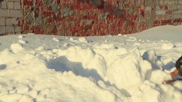 A wooden shovel close-up clears a large snowdrift. Large snowdrifts around after a snowstorm, sunny day. City life, heavy snowfall. UHD 4K.
