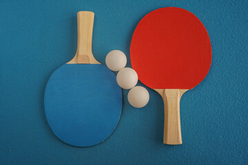 Red and blue table tennis or ping pong rackets and three balls lie on a blue background with a close-up view from above. Game for leisure. Sport equipment. International competition. Table tennis. 
