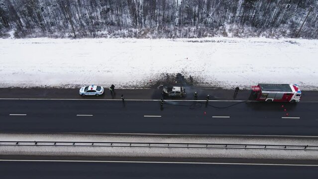 Misfortune - a burned-out car on the edge of a motorway, aerial view. Near the fire and police cars. Help and rescue concept, 911 service. White snow on the side of the road. UHD 4K