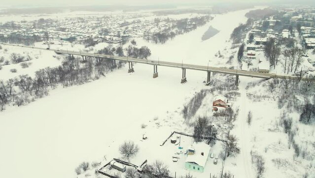 Aerial view of a frozen river in winter with a road bridge in the suburbs. Central Russia. Fabulous winter natural landscape, background, screensaver, footage, video. UHD 4K.