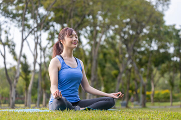 Fototapeta na wymiar Young Asian woman in yoga suit relaxingly practicing meditation in the forest to attain happiness from inner peace wisdom for breathing exercise, healthy mind and soul concept