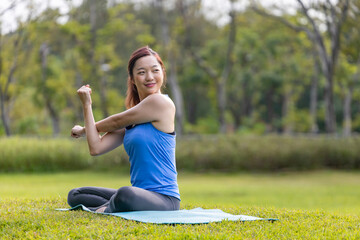 Asian woman relaxingly practicing arm and shoulder stretching yoga inside the public park for cool down after exercise in the public park