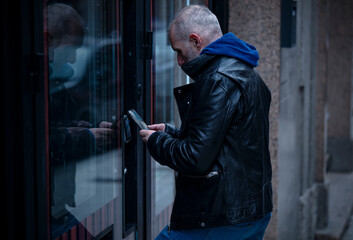 Adult man buying on automatic vending machine with mobile phone on street.