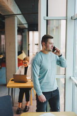 Fototapeta premium Business man, manager looking out of window in deep thought, standing at workplace with phone in office, thinking about future of company, thinking about solution for work task