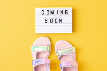 Coming soon. Motivational quote on lightbox and stylish holographic sandals on yellow background. Top view, Flat lay. Creative inspirational summer concept
