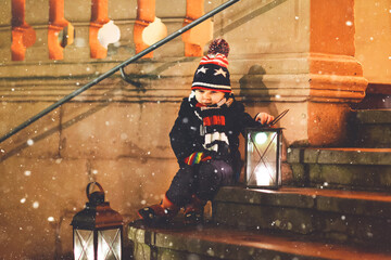Little cute kid boy with with a light lantern on stairs near church. Happy child on Christmas...