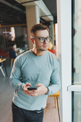 Business man, manager looking out of window in deep thought, standing at workplace with phone in office, thinking about future of company, thinking about solution for work task