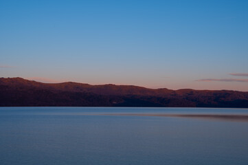山が朝焼けに赤く染まる夜明けの湖の風景。