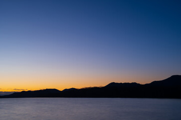 夜明けの空は美しいグラデーションに山のシルエットが際立つ湖の風景。