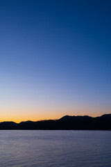 夜明けの空は美しいグラデーションに山のシルエットが際立つ湖の風景。