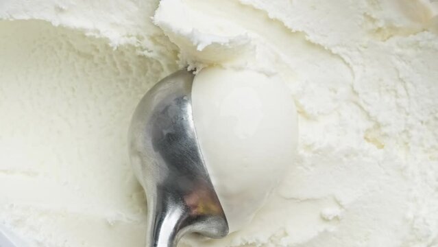 Vanilla ice cream scooping out of container by spoon. Delicious dessert. Surface of white ice cream. Close-up in 4K, UHD