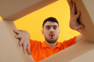 Concept of delivery, gift, surprise, young man look in to cardboard box on yellow background