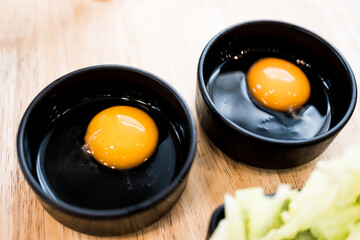 Two raw eggs in a black bowl on wood table