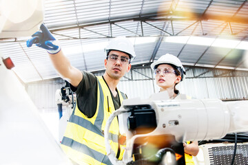 Architect team. Male and female electronic technicians operating electric welding robot arms in factory warehouse. Automated testing by industrial circuit experts consults and guides safe operation.