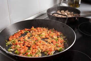 Pan for paellas with poached vegetables, in the background another pan with meat on the hob in the...