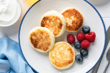 Sweet breakfast cheese pancakes or fritters Syrniki served with berries on white plate, top view