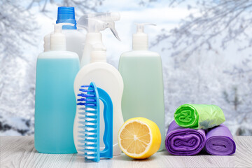Bottles of dishwashing liquid, brush and lemon with winter on background.