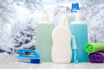 Bottles of dishwashing liquid, brushes and sponges with winter on background.