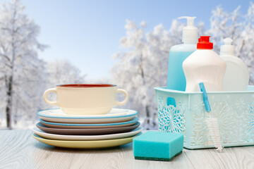 Bottles of dishwashing liquid in basket and plates with winter on background.